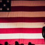 Man Standing On Stage Facing An American Flag - Man Standing On Stage Facing An American Flag