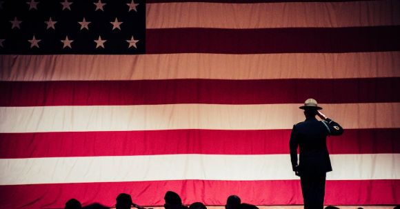 Man Standing On Stage Facing An American Flag - Man Standing On Stage Facing An American Flag