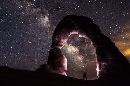 Galaxies - Person Standing Under A Rock Formation On A Starry Night