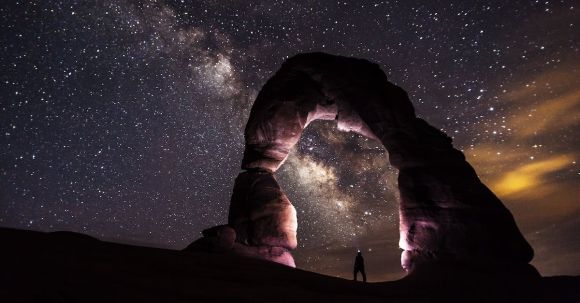 Galaxies - Person Standing Under A Rock Formation On A Starry Night